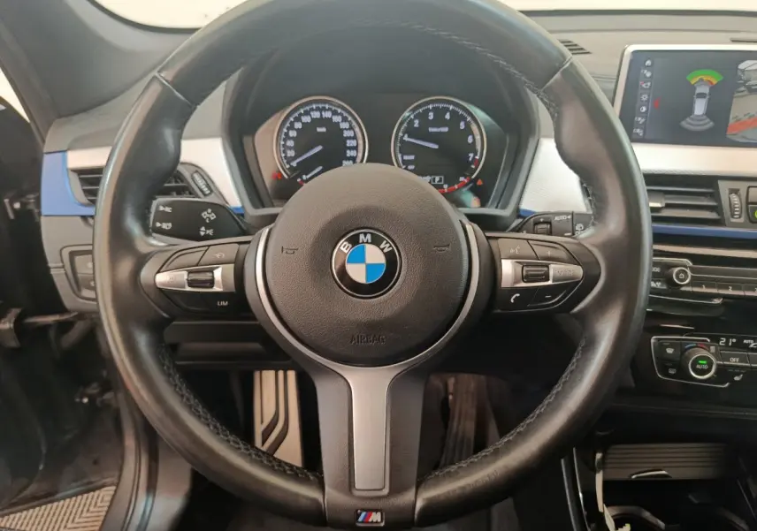 Volant cuir noir BMW M Sport avec commandes intégrées, tableau de bord et écran tactile affichant l'aide au stationnement.
