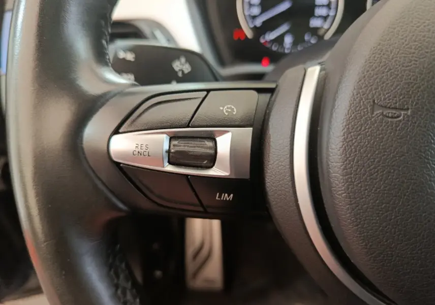 Gros plan sur les commandes de régulateur de vitesse côté gauche du volant cuir noir d'une BMW X1 sDrive18i M Sport 2019.