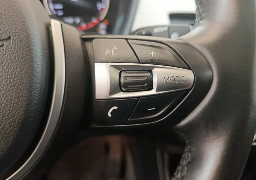 Gros plan sur les commandes du volant côté gauche en cuir noir du BMW X1 sDrive18i M Sport 2019.