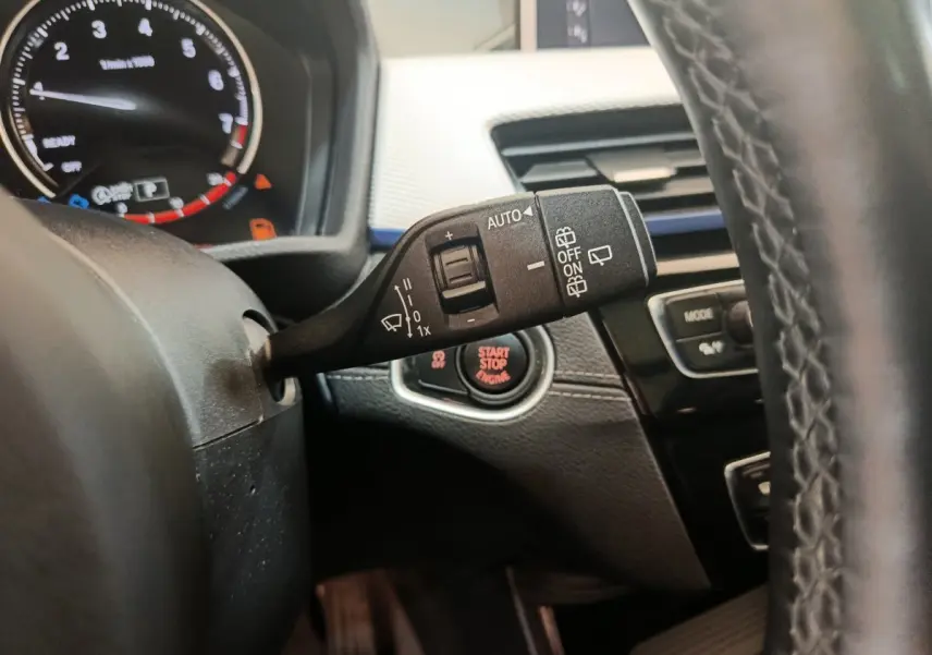 Gros plan sur la commande d'essuie-glace et le bouton start/stop du tableau de bord noir d'une BMW X1 sDrive18i M Sport 2019.