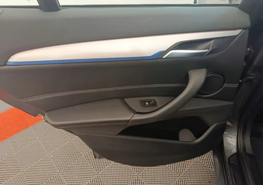 Vue intérieure côté gauche de la porte d'une BMW X1 sDrive18i M Sport 2019 avec garniture noire et insert blanc-bleu.
