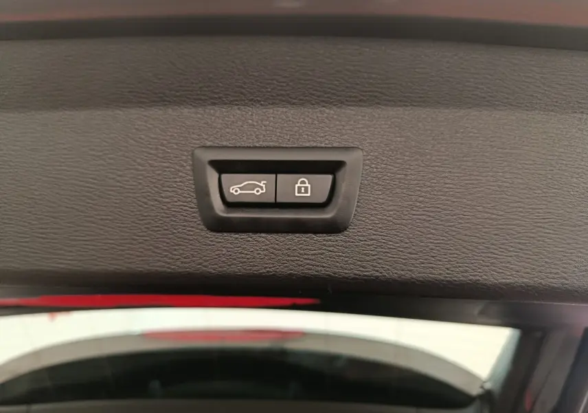 Gros plan sur les boutons d'ouverture et de verrouillage du coffre d'un BMW X1 sDrive18i M Sport 2019, intérieur noir.