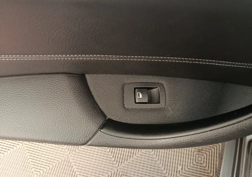 Bouton de commande de lève-vitre sur la porte intérieure côté conducteur d'une BMW X1 sDrive18i M Sport 2019, finition noire.