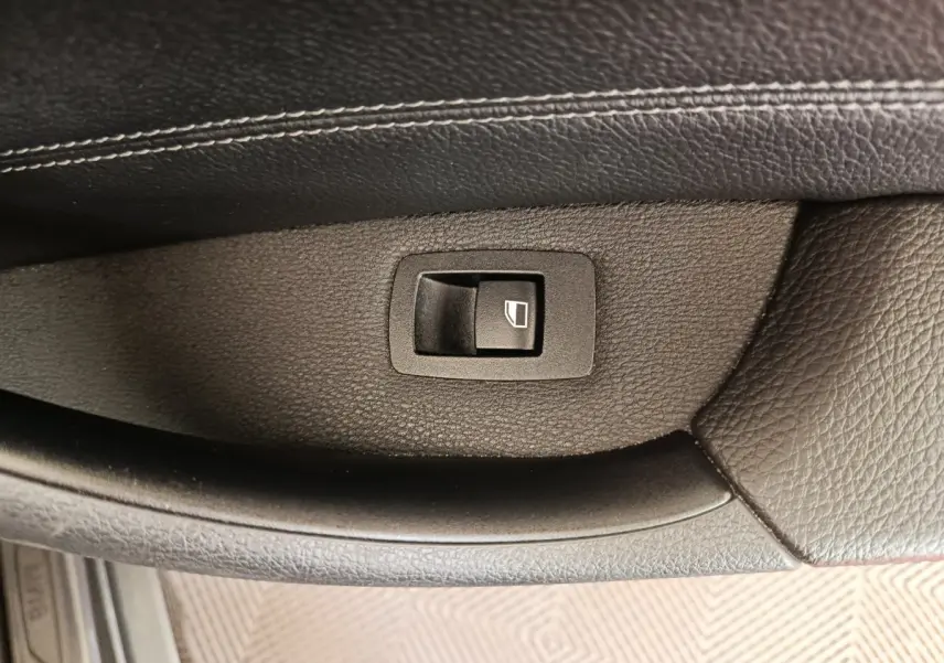 Gros plan sur le bouton de commande de lève-vitre en plastique noir sur la porte intérieure en cuir noir d'une BMW X1 sDrive18i M Sport 2019.