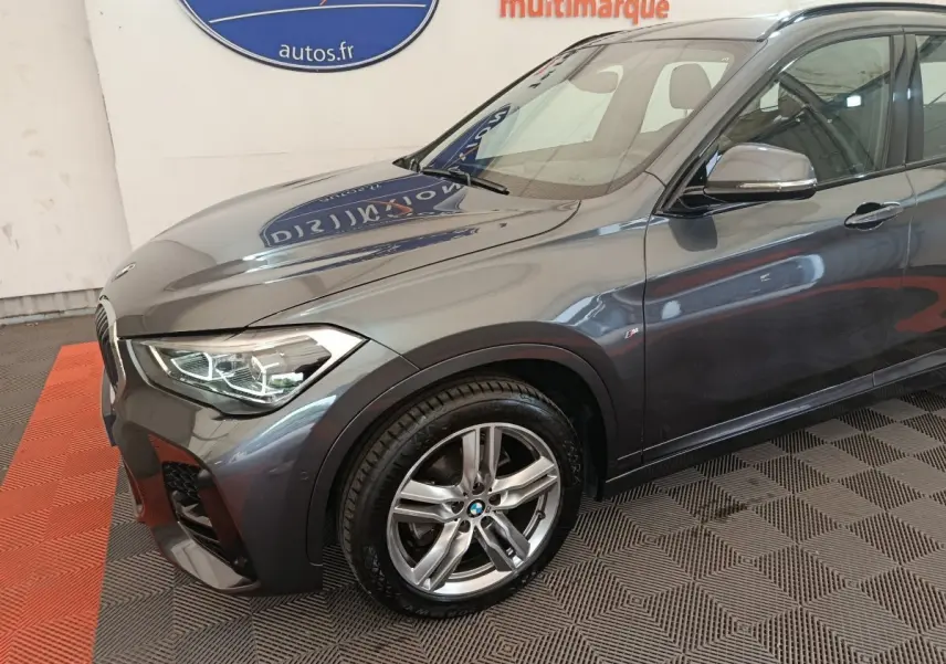 Vue 3/4 avant droit d'un BMW X1 sDrive18i M Sport gris métallisé avec jantes alliage et phares LED allumés.
