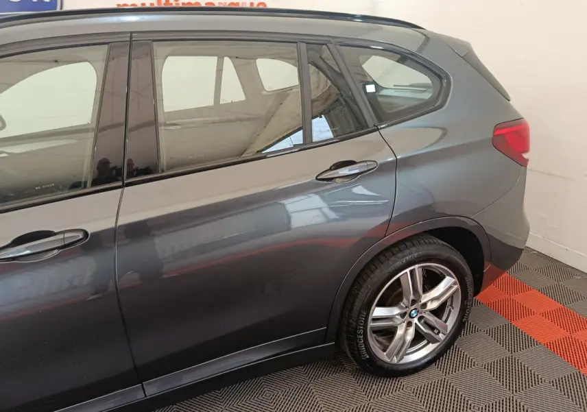 Vue latérale droite sur l'arrière d'un BMW X1 gris métallisé avec jantes alliage et feux arrière visibles.