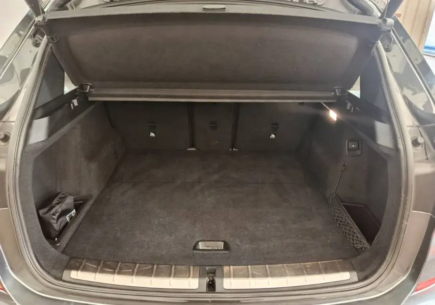 Coffre ouvert vu de l'arrière d'un BMW X1 sDrive18i M Sport 2019 gris foncé avec tapis noir et filet latéral.