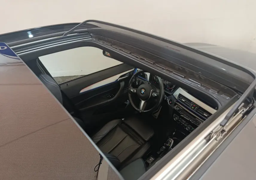 Vue plongeante sur l'intérieur noir d'une BMW X1 sDrive18i M Sport 2019 avec toit ouvrant panoramique ouvert.