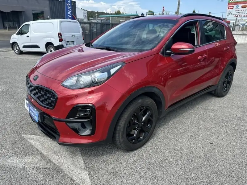 KIA SPORTAGE rouge métal vu en 3/4 avant droit, avec jantes noires et détails Black Edition visibles sur carrosserie.