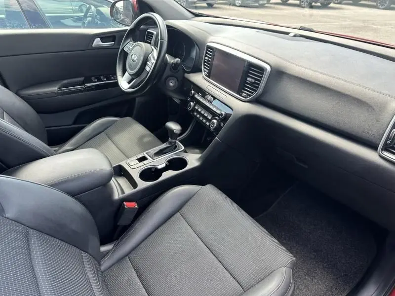 Intérieur du Kia Sportage 2021 en rouge métal, vue côté conducteur montrant tableau de bord et console centrale noire.