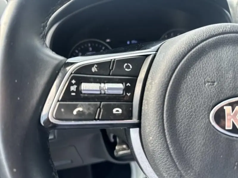 Gros plan sur les commandes gauche du volant du KIA SPORTAGE 2021, cuir noir et boutons multifonctions visibles.
