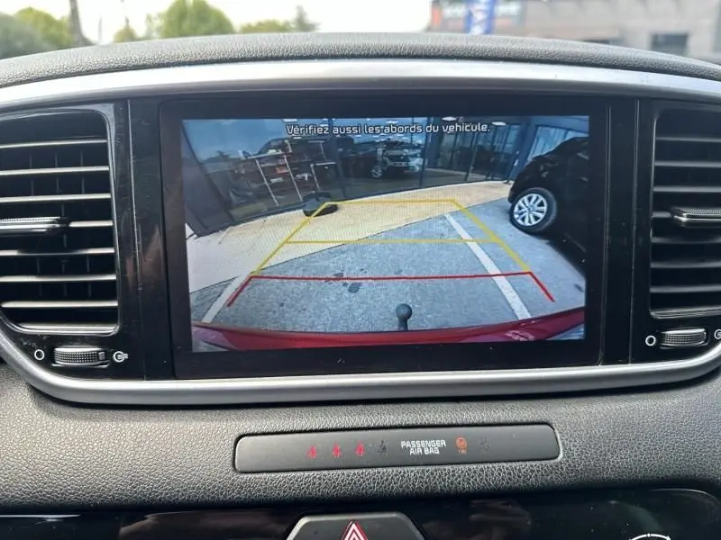 Vue depuis la caméra de recul du Kia Sportage rouge métal 2021, affichée sur l'écran central du tableau de bord.