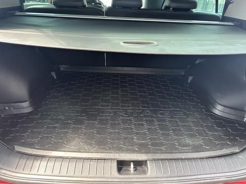Coffre ouvert du Kia Sportage 2021 rouge métal, vue arrière montrant le tapis de coffre noir avec logo "SPORTAGE".