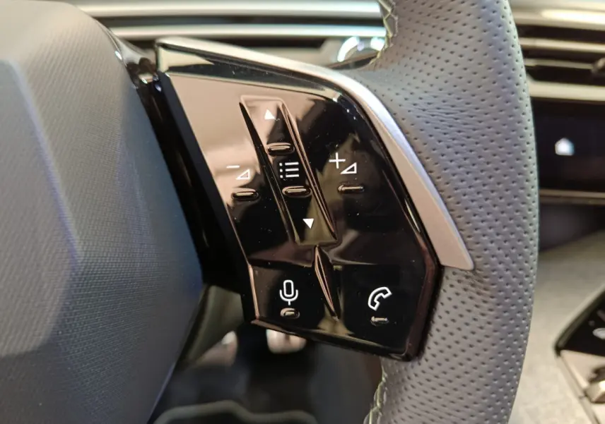 Gros plan sur les commandes tactiles noires du volant cuir perforé du Peugeot 3008 blanc hybride 2025.