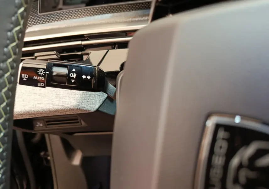 Gros plan sur la manette des feux à gauche du volant gris clair du Peugeot 3008 blanc hybride 2025.