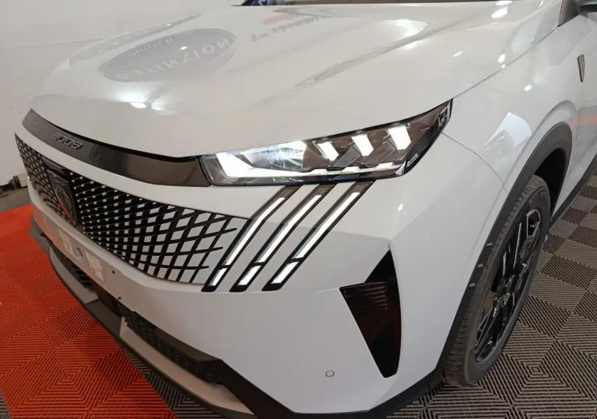 Vue 3/4 avant droit du Peugeot 3008 blanc, mettant en valeur ses phares LED et la calandre au design géométrique distinctif.