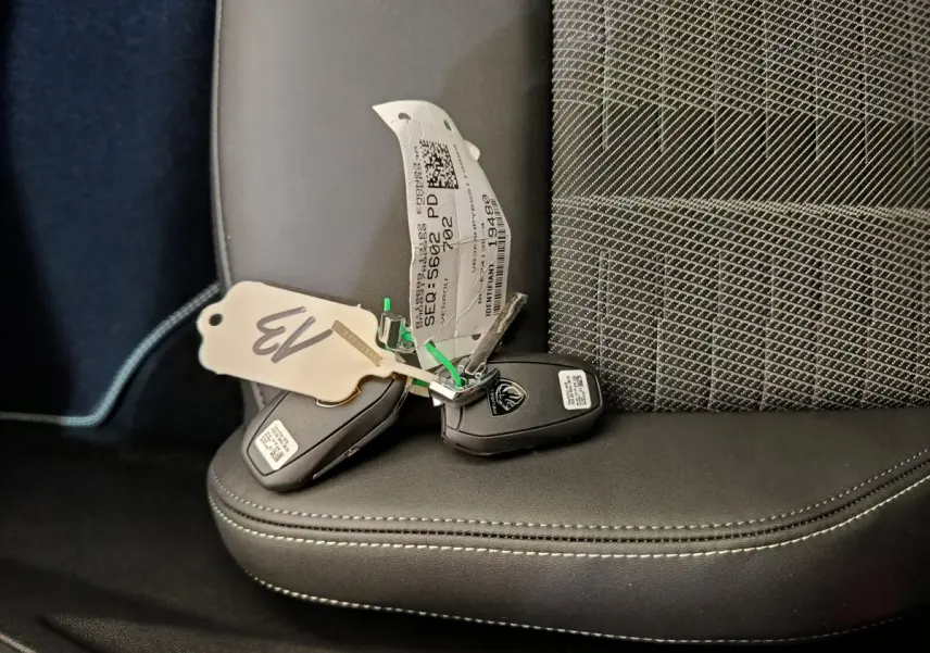 Gros plan sur deux clés Peugeot posées sur un siège avant en cuir noir et tissu gris à motifs.