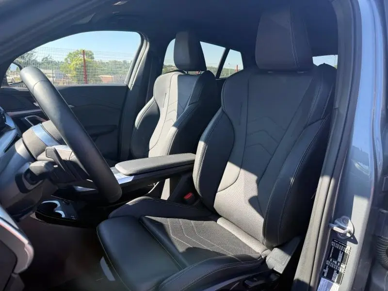 Vue intérieure côté conducteur du BMW X2 sDrive20dA 2025, sièges sport en cuir noir avec accoudoir central.