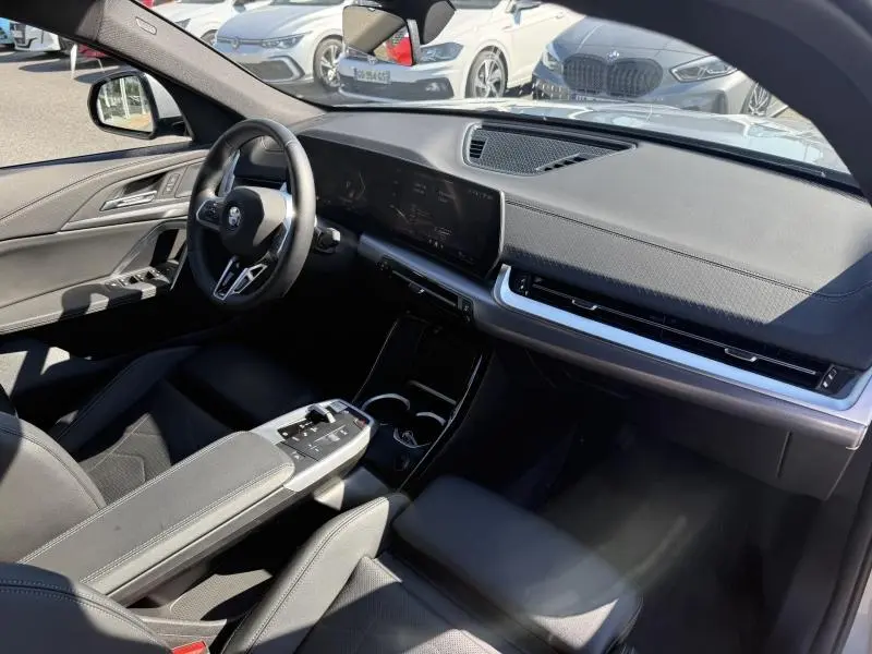 Vue intérieure côté conducteur du BMW X2 M Sport 2025 avec tableau de bord noir et écran tactile panoramique.