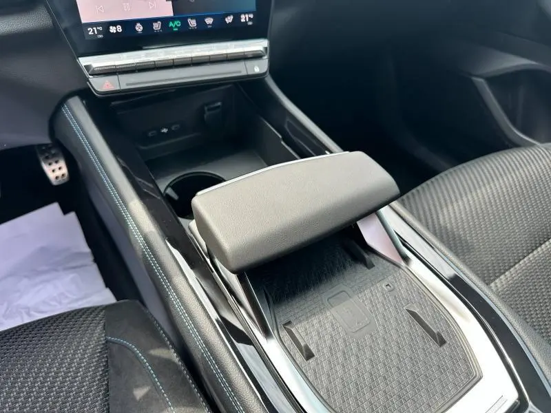 Vue rapprochée de la console centrale et accoudoir gris du Renault Austral hybride 2025 avec surpiqûres bleues.