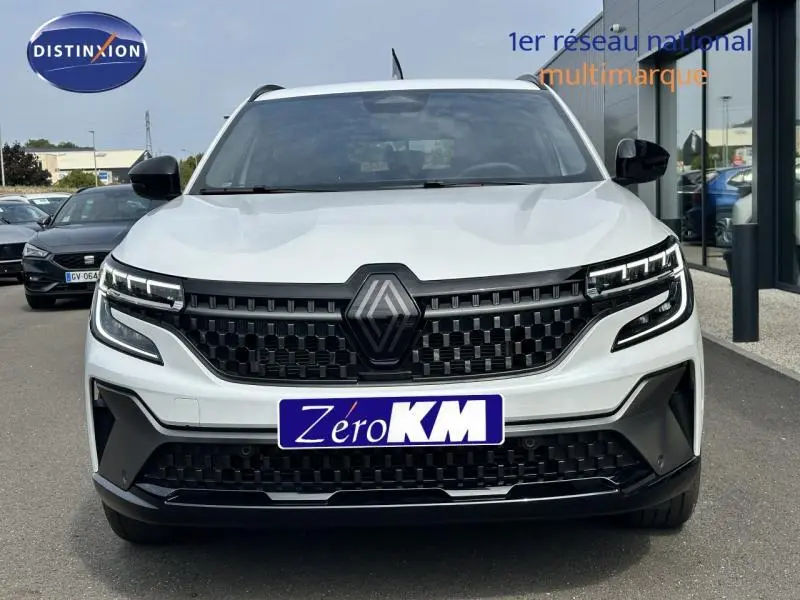 Vue frontale d'un Renault Austral gris avec calandre noire et phares LED distinctifs, sur parking extérieur.