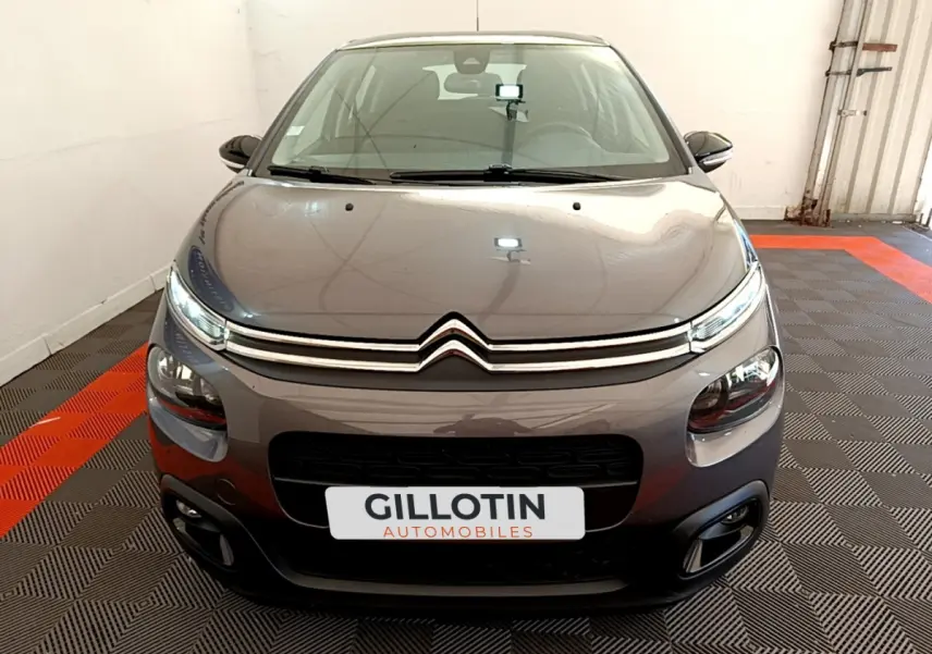 Vue frontale d'une Citroën C3 gris foncé avec phares LED et calandre chromée dans un showroom.