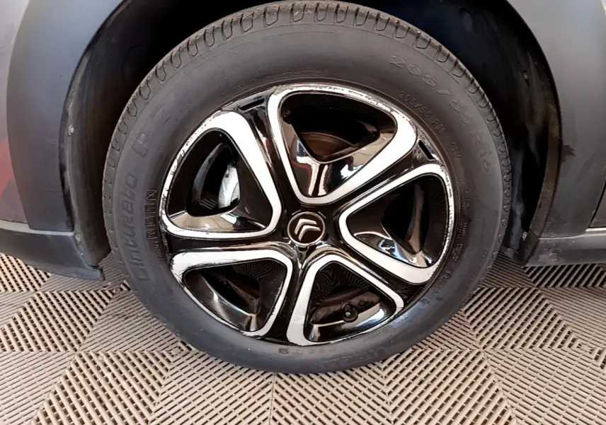 Gros plan sur la roue avant gauche d'une Citroën C3 gris foncé, mettant en valeur la jante noire et chromée au design moderne.