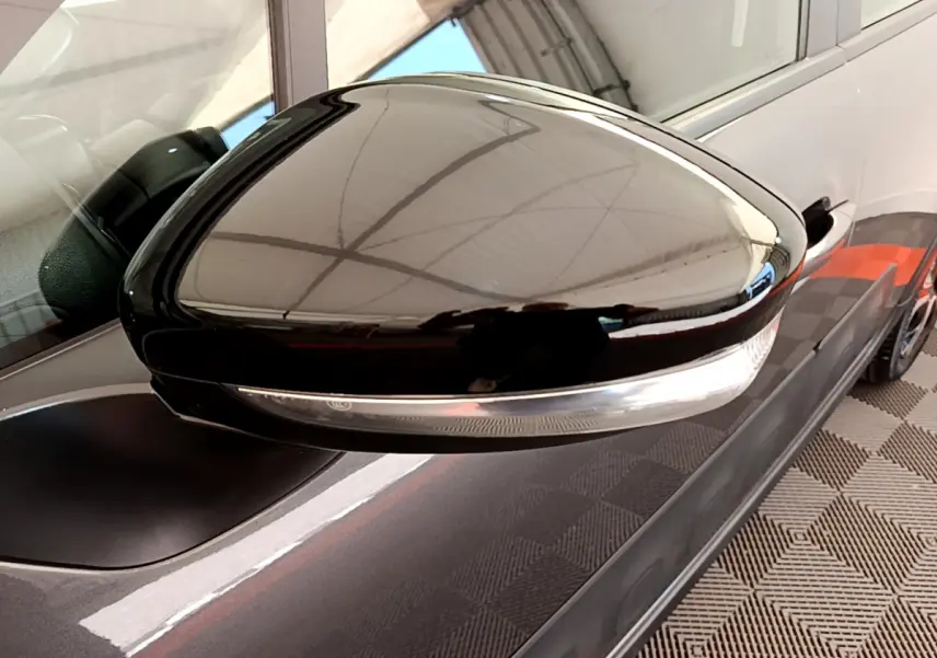Rétroviseur noir brillant côté conducteur d'une Citroën C3 gris foncé vue de près sur fond intérieur.