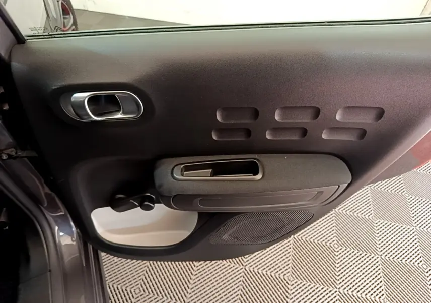 Détail de la porte côté gauche de la Citroën C3 gris foncé avec poignée intérieure et commandes manuelles.