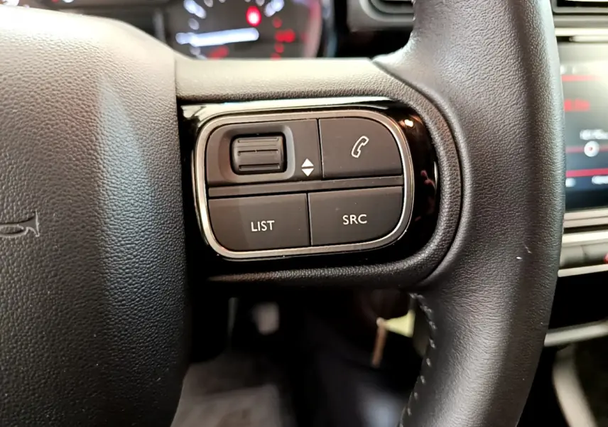 Gros plan sur les commandes gauche du volant cuir noir de la Citroën C3 gris foncé, avec boutons de téléphone et audio.