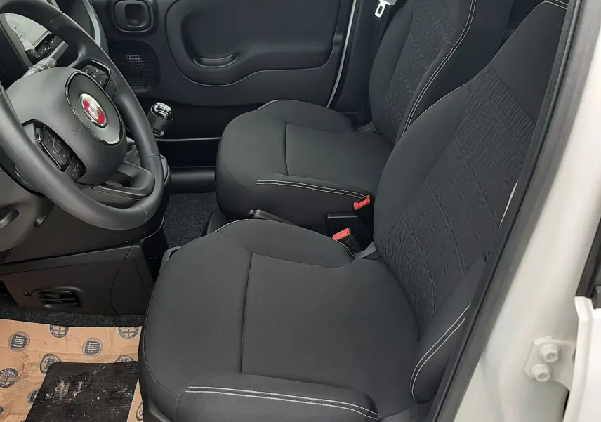 Vue intérieure côté conducteur de la Fiat Panda blanc gelato 2025, sièges tissu noir avec volant multifonction.