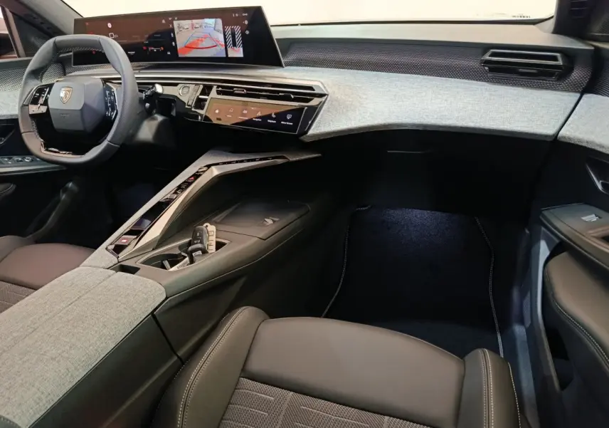 Intérieur du Peugeot 3008 2025 vu côté passager, tableau de bord moderne avec écran tactile large et sellerie grise et noire.