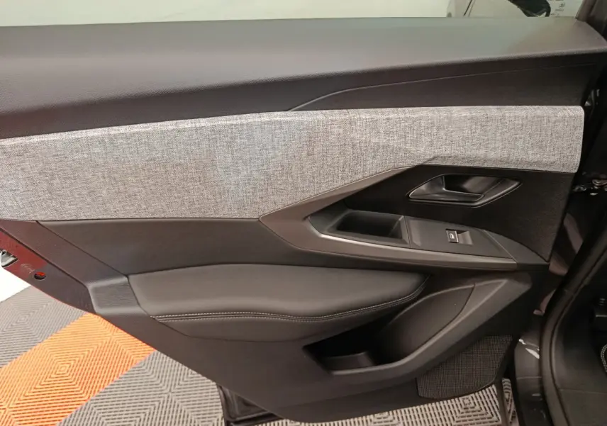 Gros plan sur la porte intérieure côté gauche du Peugeot 3008 noir, avec garniture tissu gris et commandes électriques.