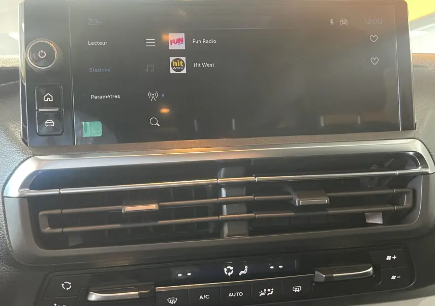 Vue rapprochée de l'écran tactile et de la console centrale du Peugeot Traveller 2026, avec commandes climatisation et radio affichée.