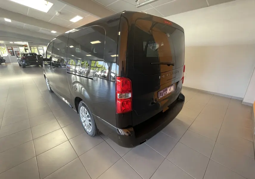 Vue 3/4 arrière droite du Peugeot Traveller noir 2026 en showroom, avec feux arrière et vitres teintées visibles.