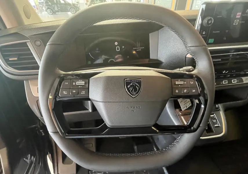 Vue rapprochée du volant cuir noir du Peugeot Traveller 2026 avec commandes intégrées et tableau de bord digital.