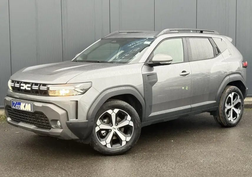 Dacia Duster gris schiste en 3/4 avant droit, avec jantes alliage diamantées et barres de toit noires.