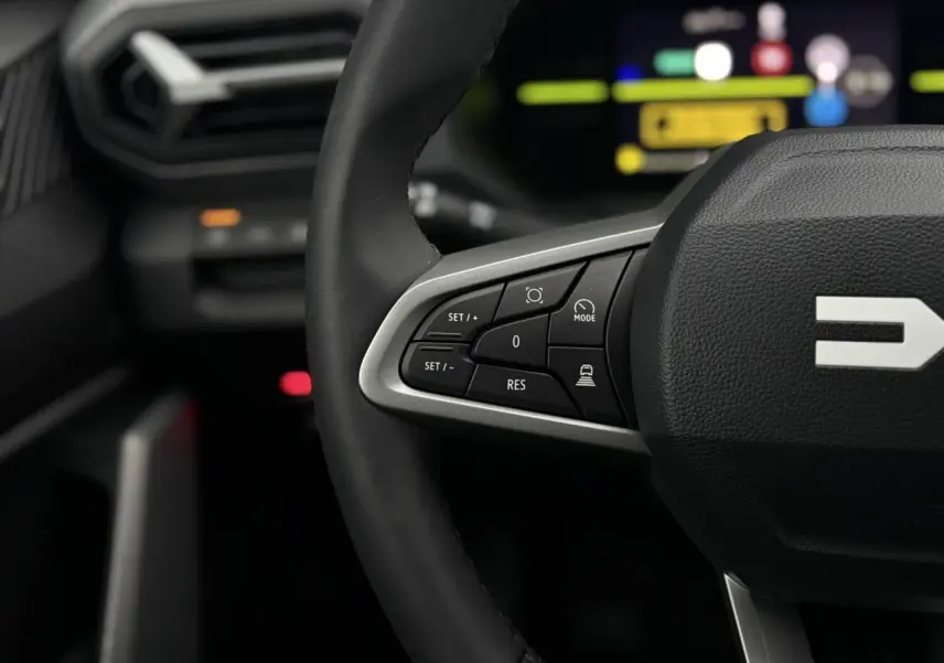 Gros plan sur le volant noir du Dacia Duster 2026 avec commandes multifonctions et tableau de bord digital flou en arrière-plan.