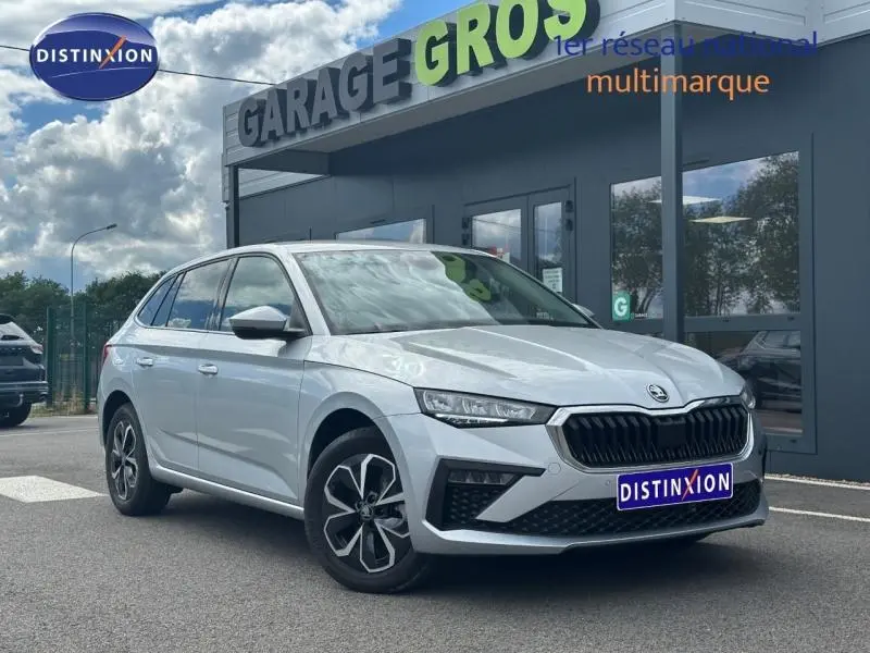 Vue 3/4 avant droite d'une Skoda Scala gris argent métallisé avec calandre chromée et jantes alu devant un garage.