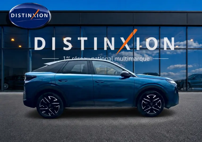 Profil côté gauche d’un Peugeot 3008 bleu 2025 avec jantes alu noires et toit noir devant un bâtiment vitré.