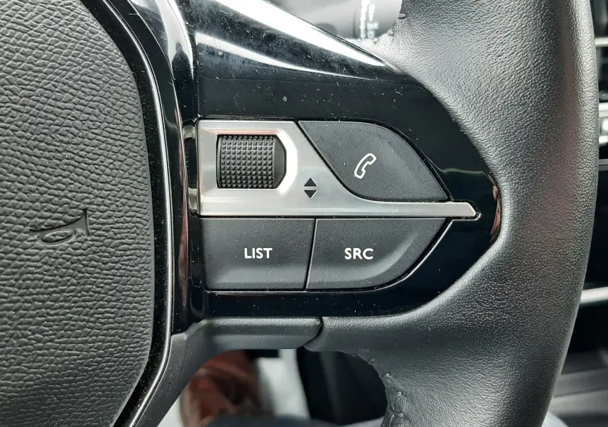 Gros plan sur les commandes gauche du volant en cuir noir du Peugeot 208 gris sélénium, boutons SRC et LIST visibles.