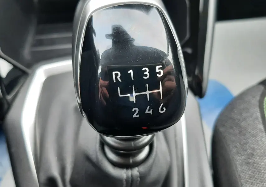 Gros plan sur le levier de vitesses manuel noir brillant de la Peugeot 208 2024, avec marquage des six rapports et marche arrière.