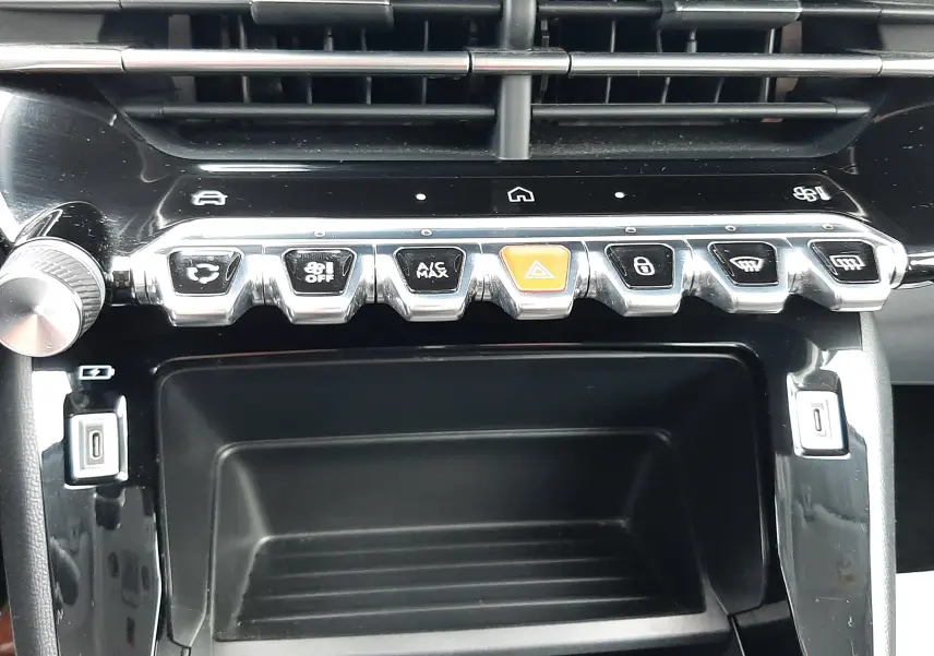 Vue rapprochée de la console centrale noire brillante de la Peugeot 208 2024 avec boutons de commande chromés et voyants lumineux.
