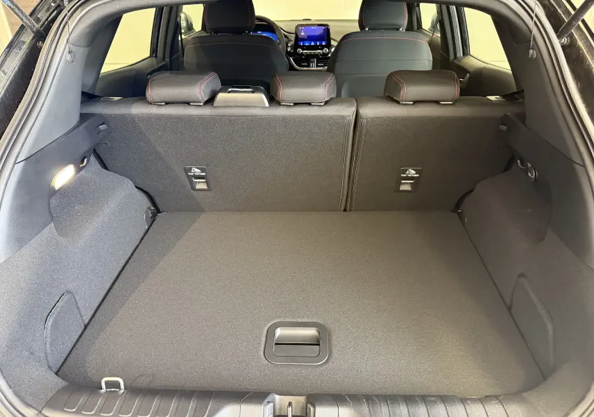 Coffre ouvert du Ford Puma noir agate, vue arrière montrant l’espace de chargement et les sièges arrière avec surpiqûres rouges.