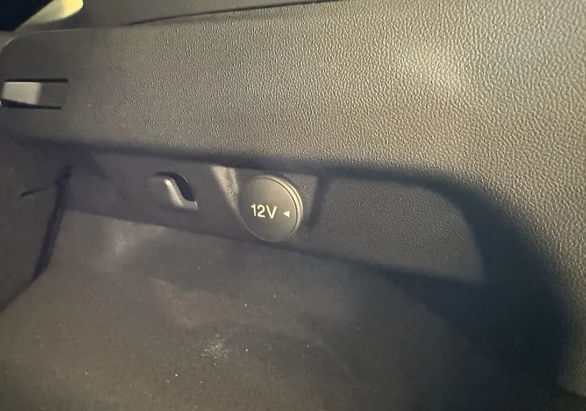 Prise 12V intégrée dans le coffre du Ford Puma noir Agate, vue rapprochée sur la console latérale intérieure.