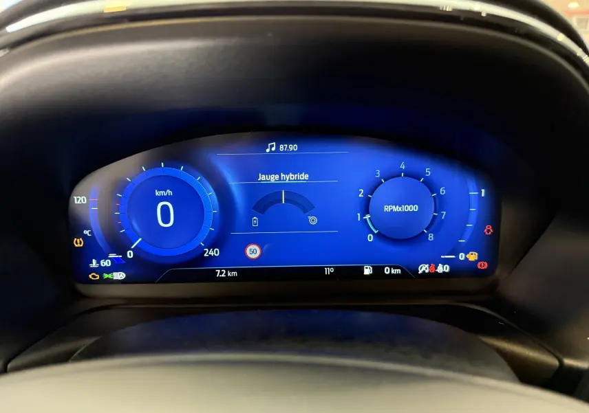 Vue rapprochée du tableau de bord numérique bleu du Ford Puma 1.0 EcoBoost MHEV 155ch noir agate, affichant vitesse et jauge hybride.