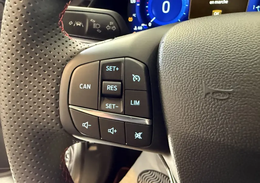 Gros plan sur le volant perforé avec commandes intégrées du Ford Puma noir Agate, tableau de bord digital en arrière-plan.