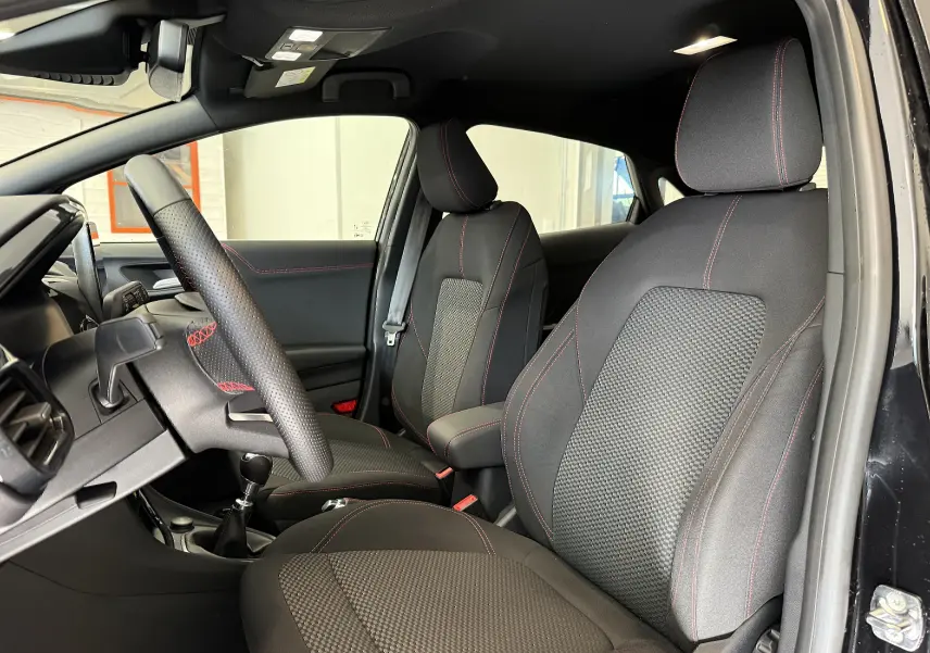Vue intérieure côté gauche du Ford Puma noir agate 2022, mettant en valeur les sièges avec surpiqûres rouges et volant perforé.