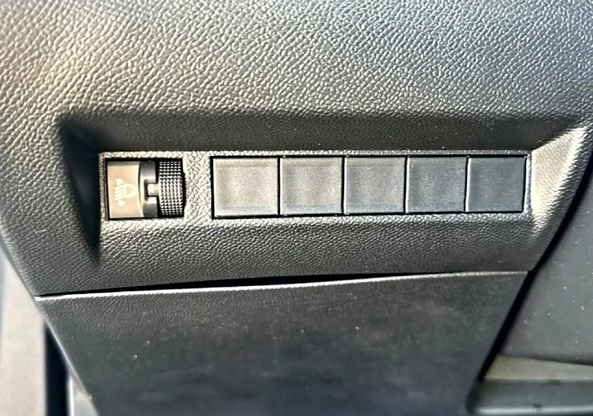 Détail du tableau de bord noir du Peugeot 2008 2025, montrant la molette de réglage des phares et cinq boutons inactifs.