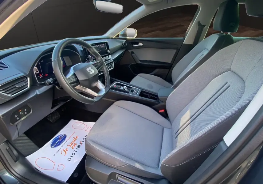 Vue intérieure côté conducteur de la SEAT Leon IV 2024 avec sièges tissu gris clair et tableau de bord moderne.